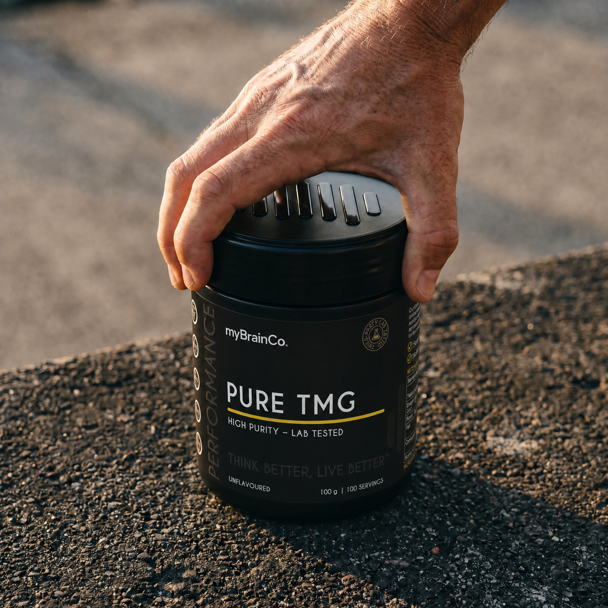 Hand holding a black container labeled 'PURE TMG' by myBrainCo on a textured surface.