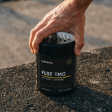 Hand holding a black container labeled 'PURE TMG' by myBrainCo on a textured surface. thumbnail
